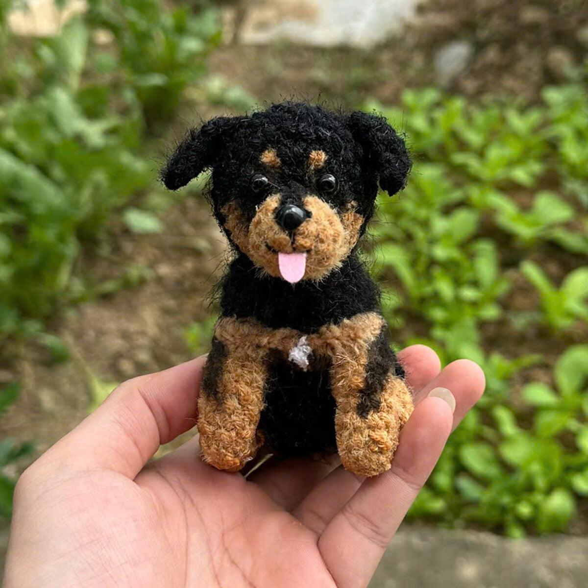 The same Rottweiler as a hand-crocheted doll charm, held in a hand